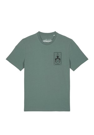 T-shirt vert à manches courtes avec un petit motif noir de carte de tarot sur la poitrine montrant une femme et un lion avec le mot "STRENGTH."