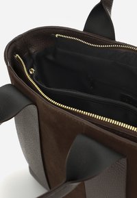 Borsa tote in pelle marrone con chiusura a zip, caratterizzata da dettagli in suède, un interno nero e doppie maniglie superiori. Hardware in tonalità oro visibile.