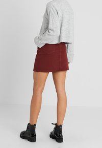 Burgundy denim minikjol med en figursydd design, två bakfickor och en lätt frans vid fållen, i kombination med en grå kortärmad tröja och svarta stövlar.