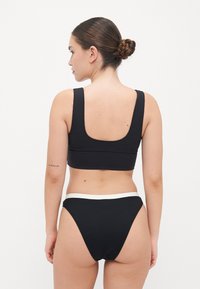 Black swimsuit top with a square neckline and thick straps, paired with black textured bikini bottoms featuring a white elastic waistband.