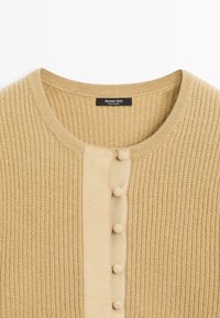 Beige gebreid vest met een gestructureerd patroon, een glad voorpand, een ronde halslijn en kleine met stof bedekte knopen in het midden.