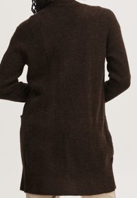 Cárdigan de punto marrón con un corte relajado, mangas largas y bolsillos laterales; tejido texturizado con una apariencia suave y esponjosa.