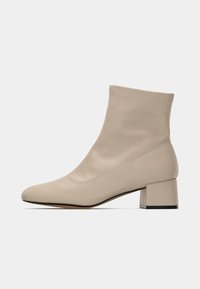 Cizmă de sosete bej, până la jumătatea gambei, cu vârf rotund și toc gros, pe un fundal alb, prezentată din partea stângă.