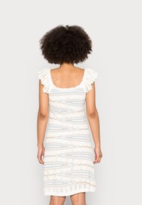 Vestito bianco a maglia con un motivo a strisce ondulate in blu e beige, con scollatura quadrata e maniche a volant. Dettagli in pizzo testurizzato all'orlo.