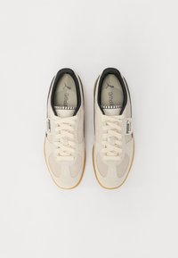 Beżowe zamszowe sneakersy z czarnym wykończeniem, sznurowany design, gumowa podeszwa w kolorze gumy oraz metki z logo po bokach z fakturowanym wzorem.