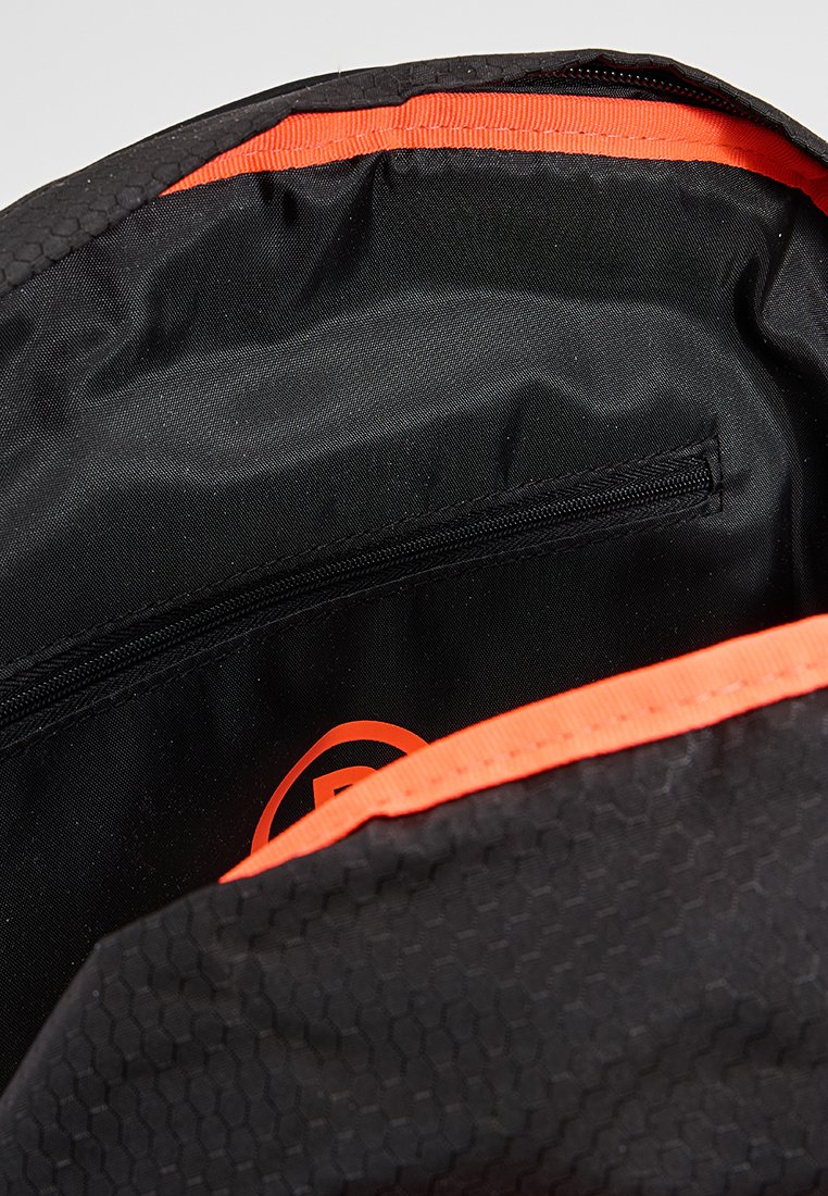 Schwarzer Rucksack-Innenraum mit einem strukturierten hexagonalen Muster, orangefarbener Einfassung, einem Reißverschlussfach und einem sichtbaren Logo. Glatte Stoffauskleidung.