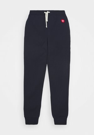 Marineblaue Jogginghose mit weißem Kordelzugbund und kleinem rotem rundem Logo an der rechten Hüfte.