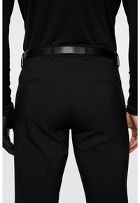 Svarta byxor med en slät textur, bälteshällor och två bakfickor. Midjan är smal och den övergripande designen är skräddarsydd.