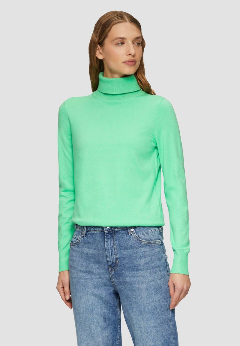 Mintgroene coltrui van zacht breiwerk, met lange mouwen en een aansluitende pasvorm. Gecombineerd met lichtblauwe jeans.