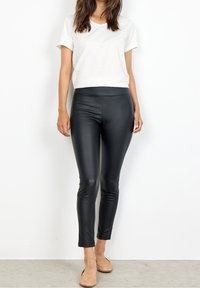 Svart fusk läder leggings med hög midja, tillsammans med en vit kortärmad T-shirt och beige ballerinas. Slät textur, figurnära design.