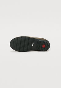 Sole in gomma nera con modelli di battistrada orizzontali e un logo circolare rosso. Presenta sezioni texture e lisce per una migliore aderenza.