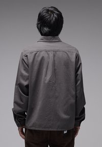 Γκρι πουκάμισο με μακριά μανίκια, γιακά, μανσέτες με κουμπιά και άνετη εφαρμογή. Διαθέτει λεία υφή και μία ραφή στην πλάτη.