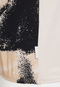 Beżowa i czarna bluzka z teksturowanym nadrukiem w formie plamy, gładkim materiałem, metką na bocznym szwie oraz zaokrąglonym dołem.