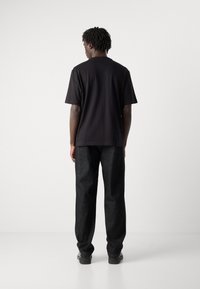 Camiseta negra de manga corta con corte recto, combinada con jeans de mezclilla oscuros y holgados. La textura parece suave y casual.