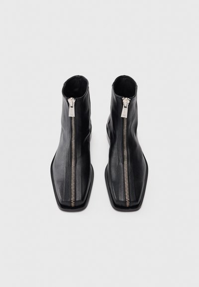 Botas de cuero negras hasta el tobillo con punta cuadrada y una cremallera plateada de longitud completa en la parte delantera. Textura suave y diseño elegante.