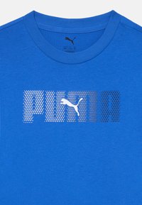 Blå bomulls-T-shirt med en framträdande vit och metallisk logotryck med en puma-silhuett i mitten. Rund halsringning och korta ärmar.
