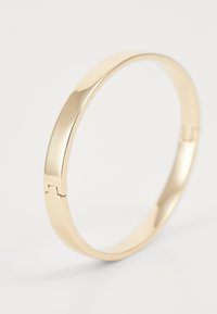 Gold metal bangle bracelet with a smooth, polished finish and a hinged clasp. Rounded shape with a minimalist design.