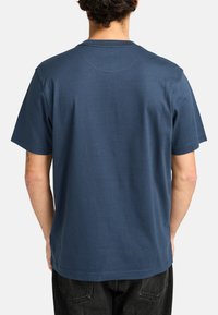Camiseta de algodón azul marino con mangas cortas, cuello redondo y corte relajado. Textura suave y detalle de costura mínima en la parte de atrás.
