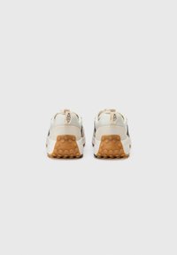Chaussures de sport avec une tige en cuir beige et en mesh, des accents foncés et une semelle en caoutchouc texturé avec des motifs circulaires distinctifs.