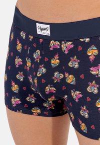 Boxer in cotone con sfondo blu scuro, caratterizzati da colori decorativi vivaci di cuori, fiamme e uccelli, rifiniti con un elastico logo.