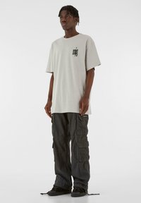Lys grå oversized t-shirt med sort logo på brystet, parret med sorte cargo bukser med flere lommer og en afslappet pasform.