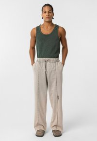 Groene geribde tanktop en lichtgrijze joggingbroek met elastische tailleband en zijnaadstiksel, gedragen met grijze instappers.