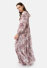 Robe maxi à manches longues florale en rose pâle avec des motifs botaniques blancs et bordeaux ; tissu léger avec un design à niveaux.