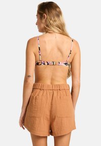 Bruna, texturerade shorts med elastisk midja och två bakfickor. Remmarna på en flerfärgad mönstrad topp syns ovanför shortsen.