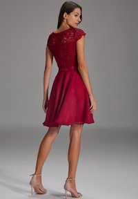 Robe bordeaux avec des manches en dentelle, corsage cintré et jupe en chiffon évasée. Présente un dos en trou de serrure et une ceinture en satin.