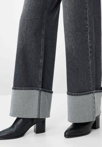 Jeans a gamba larga in denim scuro con risvolto in denim chiaro a contrasto. Presentano bordi grezzi e cuciture visibili. Abbinati a stivali neri con tacco.