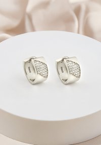 Silverörhängen i form av en båge, med en sektion av små klara ädelstenar på ena sidan. Satinfinish på insidan.