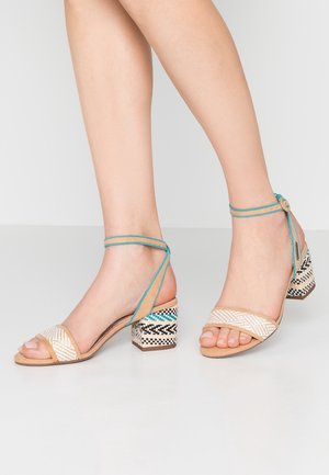 Sandalias abiertas de dedo en color beige y crema con una tira texturizada, cintas turquesas en el tobillo y un tacón bloque de varios colores con un patrón.