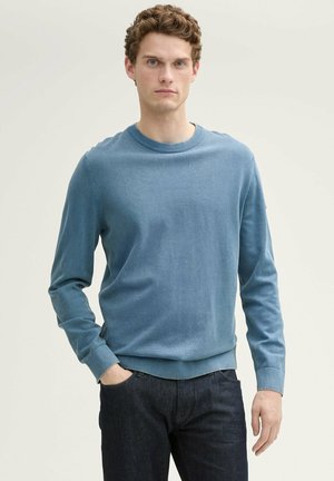 Blauwe katoenen crewneck trui met geribbelde boorden en taille, met een zachte textuur. Gecombineerd met donkere spijkerbroek. Geen zichtbare logo's.