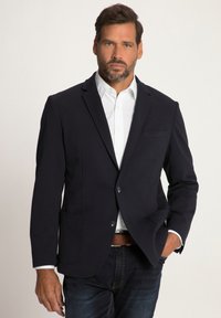 Marineblazer mit taillierter Passform, ausgestattet mit zwei Fronttaschen, einer Brusttasche und zwei Knöpfen. Getragen über einem weißen Hemd und dunklen Jeans.