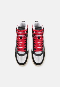 Vysoké tenisky s černobílým koženým svrškem, perforovanou špičkou, červenými tkaničkami a béžovou gumovou podrážkou.