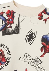 Krämfarbenes Sweatshirt mit bunten Spider-Man-Illustrationen, schwarzem Spinnenmotiv und Textelementen. Gerippter Rundhalsausschnitt und weicher Stoff.
