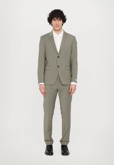 Light olive green suit with a tailored fit, single-button jacket, notch lapels, and slanted pockets paired with a white shirt and black shoes.