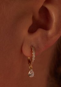 Gouden hoepeloorbellen versierd met kleine heldere stenen, met daaronder een druppelvormige kristallen hanger.