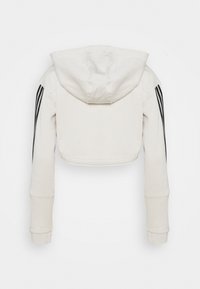 Hoodie blanc court avec trois bandes noires le long des manches, poignets longs et ajustés, et une grande capuche, vu de dos.
