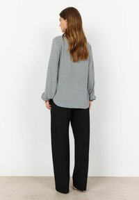 Blouse à motifs noir et blanc avec des manches longues, ourlet arrondi et coupe loose, associée à un pantalon large noir.