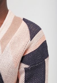 Stickad tröja med diagonala randiga mönster i mjuk beige, persika och marinblå färg. Materialet har en lös, texturerad väv.