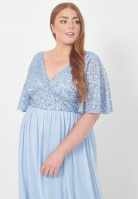 Ljusblå klänning med V-ringning, korta fladdrande ärmar och en bodice prydd med paljetter. Flödande, veckad kjol gjord av mjukt tyg.