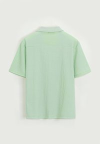 Chemise à col vert clair à manches courtes, en tissu texturé avec un motif subtil, ourlet droit et détail de empiècement au dos.