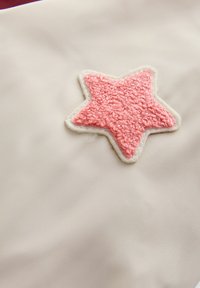 Lyserød tekstureret stjernepatch syet fast på glat beige stof med synlige syninger rundt om patchens kanter.
