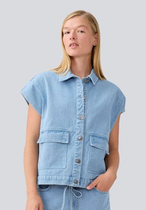 Denim ermeløs jakke i lys blå. Har knapping foran, to frontlommer og en avslappet passform med krage.