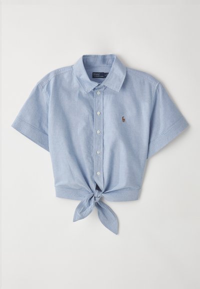 Šviesiai mėlynas, trumpomis rankovėmis marškiniai su mygtukais ir priekinio mazgo detale. Pagamintas iš minkštos medžiagos, turi klasikinį apykaklę ir mažą siuvinėtą logotipą.