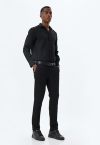 Zwarte overhemd met lange mouwen, gecombineerd met zwarte op maat gemaakte broek. Een zwarte riem en zwarte sneakers maken de look compleet. Glad textuur.