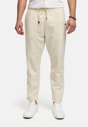 Krämfärgade joggerbyxor tillverkade av textilerad väv. Har en dragsko i midjan och sidsömmar med subtila accenter. Bärs med vita sneakers.