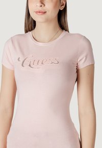 Camiseta ajustada de color rosa claro, hecha de una tela suave, con un logo de "Guess" brillante en embellecimiento decorativo en el pecho.
