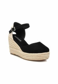 Sandalia de cuña de ante negro con plataforma de yute trenzado, correa en el tobillo y punta cerrada. La altura del tacón es de aproximadamente 7 cm.